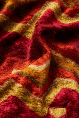 Detailaufnahme des Stoffmusters einer retro-inspirierten Samtjacke von King Louie mit Chevron-Muster in Rot-, Orange- und Gelbtönen, Modell Iris Penny Cabern.