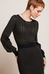 Modell mit Pixie-Frisur trägt elegantes, retro-inspiriertes Kleid mit Glockenärmeln und gold-glitzernden Details,