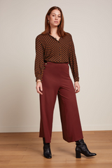 Modell trägt eine weite rostrote Culotte-Hose, kombiniert mit schwarzen Stiefeletten und einer gemusterten Retro-Bluse