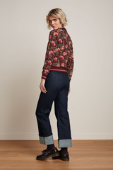 Modell trägt retro-inspirierte Zipper-Bomber-Jacke in weinrot mit floralem Muster, kombiniert mit dunkelblauen Cropped-Jeans und braunen Loafers