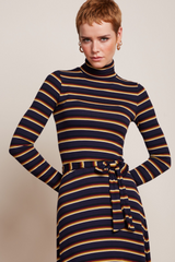 Modell mit Pixie-Frisur trägt Kurzhaar-Modell trägt Retro-inspiriertes Rollneck-Kleid auf geripptem Strickstoff mit Streifenmuster kombiniert mit Lederstiefeln