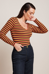 Modell trägt Anliegendes, retro-inspiriertes Longsleeve mit Streifenmuster in orangenen Farbtönen, kombiniert mit dunkelblauen Jeans