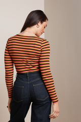 Modell trägt Anliegendes, retro-inspiriertes Longsleeve mit Streifenmuster in orangenen Farbtönen, kombiniert mit dunkelblauen Jeans